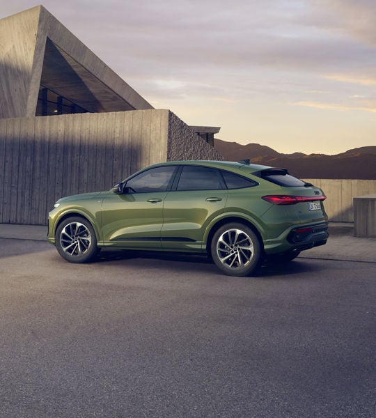 En grön Q5 Sportback ses från sidan, parkerad framför ett hus i en bergig miljö.