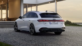 Der A5 Avant e-hybrid steht in einer schrägen Heckperspektive auf einer Kiesfläche vor einem modernen Wohnhaus.