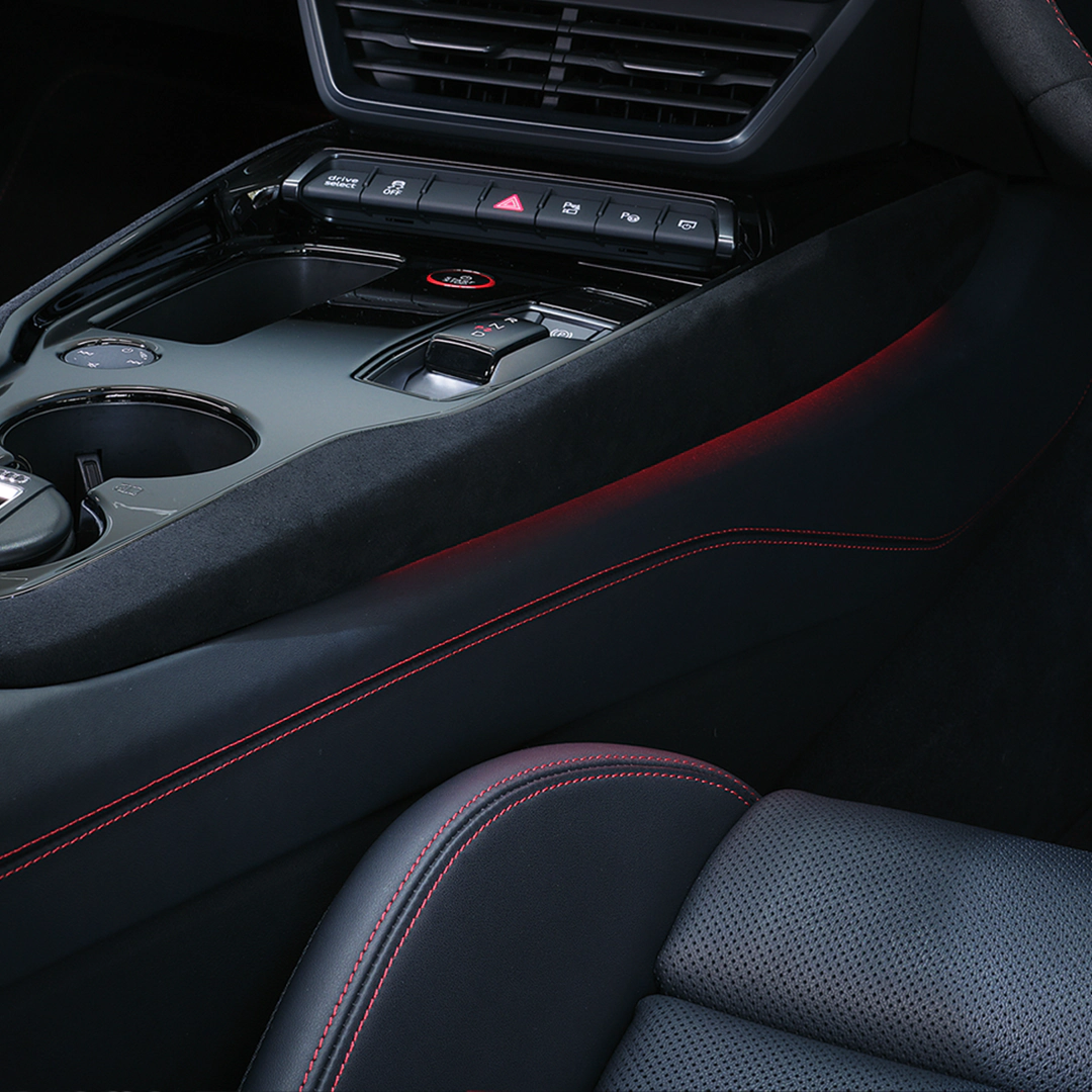 Car interior with gearstick, centre console, cup holder and part of a driver's seat. Red stitching on black leather and ambient lighting.