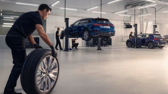 Zwei Mitarbeitende prüfen in einer Autowerkstatt ein Auto mit geöffneter Motorhaube; einer hält ein Diagnosegerät.