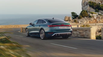 Sedan driving on a coastal road with scenic sea and cliffs in the background.