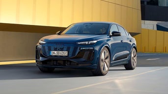 A sleek blue Audi SQ6 Sportback e-tron, showcasing modern design and bold features, parked in front of a striking yellow wall.