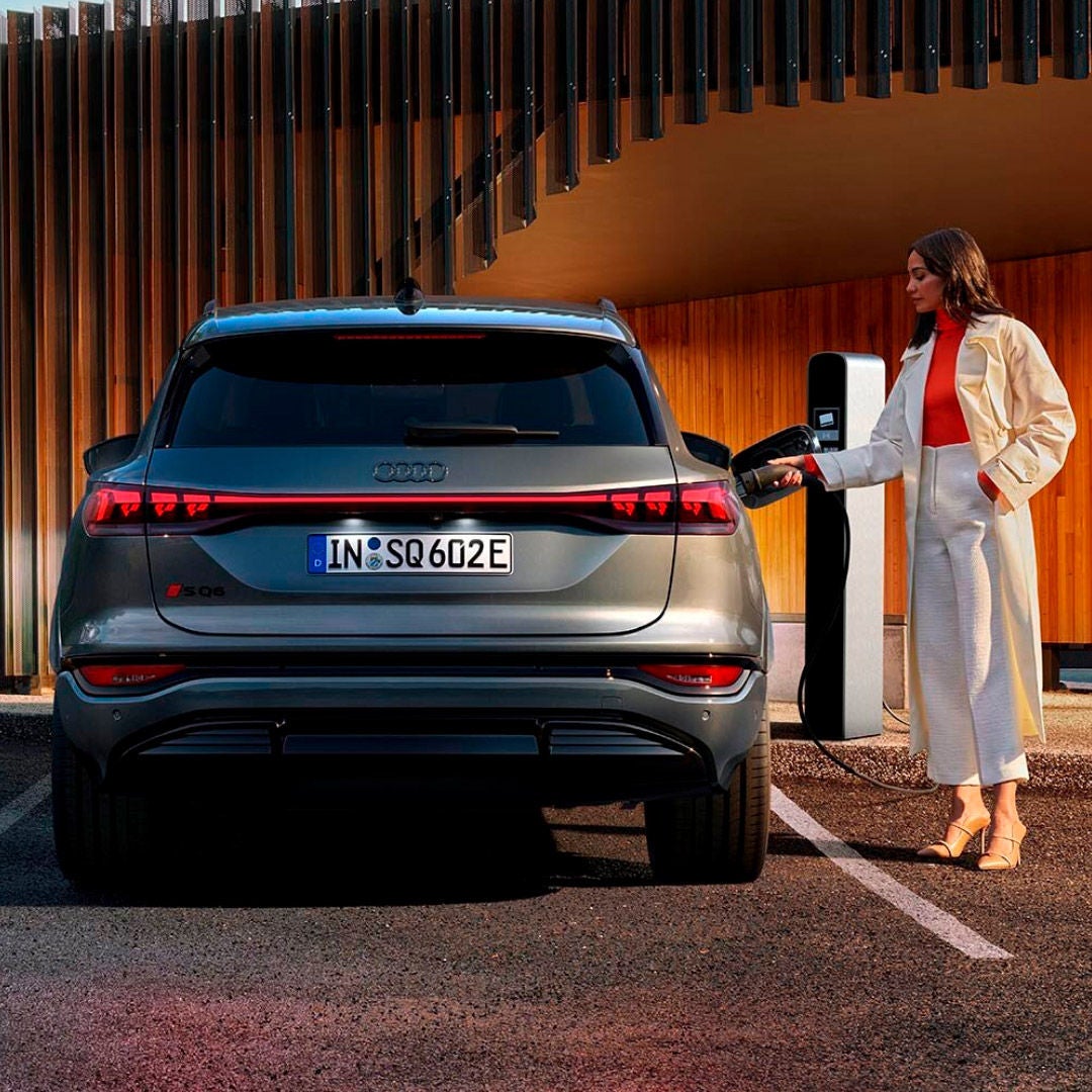 Vettura Audi SQ6 e-tron parcheggiata mentre una donna inserisce il plug di ricarica