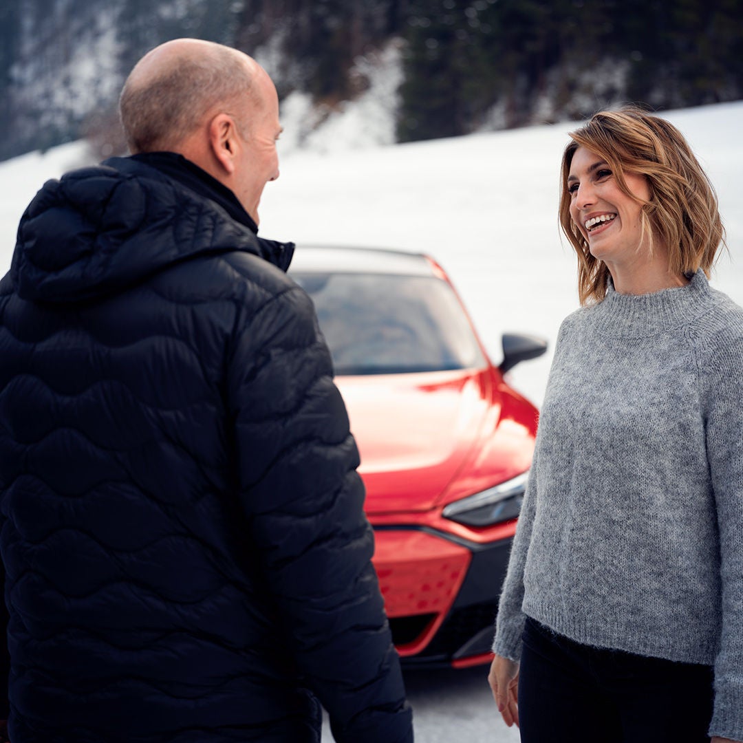 Two smiling people are standing in the snow in front of a red Audi.
