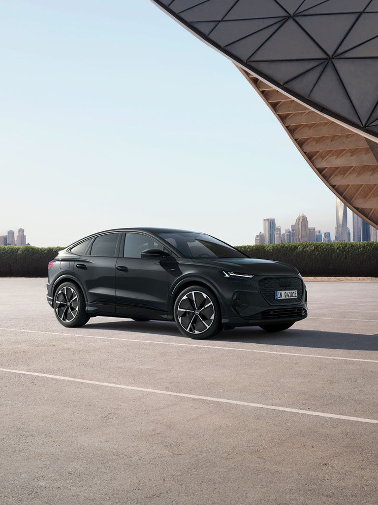 Ein schwarzer Audi Q4 Sportback e-tron steht auf einem leeren Parkplatz vor einer Stadtsilhouette.