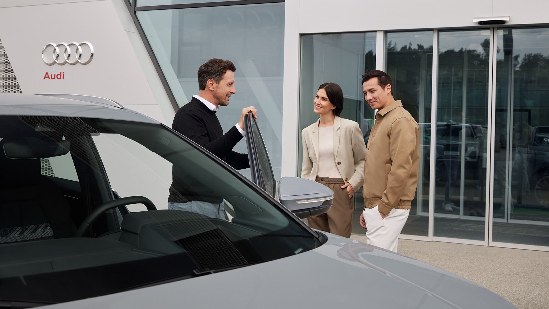 Ein junges Paar bekommt von einem Audi Verkaufsberater vor dem Autohaus das Modell gezeigt