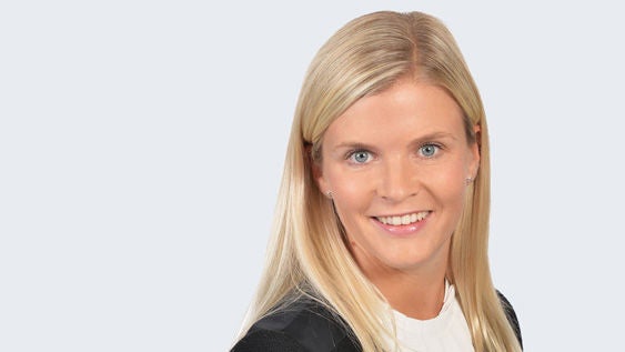 Katharina Reuther: Porträt lächelnde Frau mit blondem langen Haar vor grauem Hintergrund.