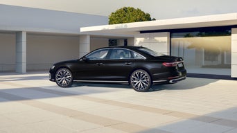 Ein schwarzer Audi A8 steht vor einem modernen, hellen Gebäude bei Tageslicht.