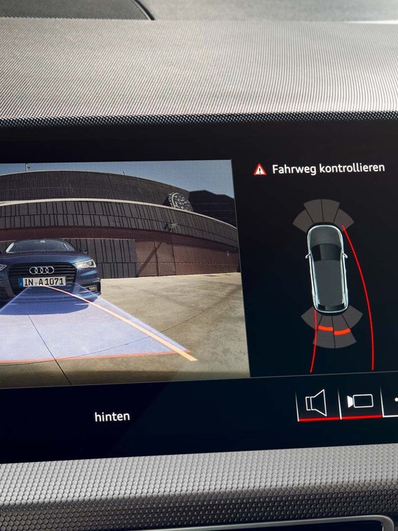Infotainmentscreen zeigt Rückfahrkamera mit Umgebung und Fahrspuranzeige sowie akustischer Warnung.