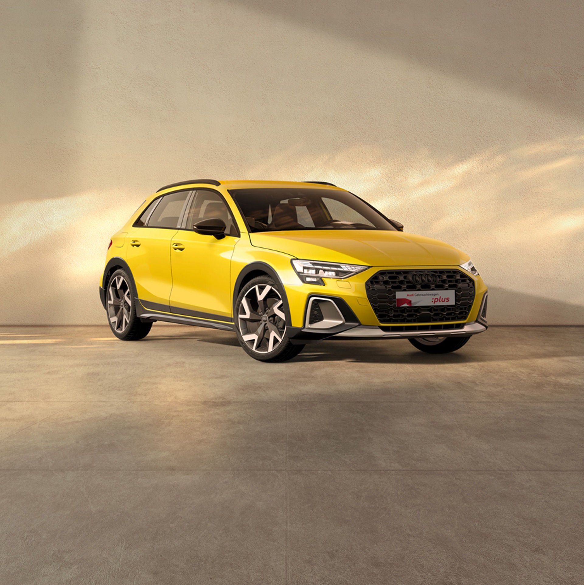 Ein gelber Audi A3 steht auf einer beigen Fläche bei einfallendem Sonnenlich. Am Rand sind Kirschblüten zu sehen.