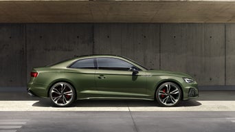 Grünes Audi Coupé seitlich vor Betonwand geparkt, rote Bremssättel sichtbar, modernes Design und sportliche Linienführung.