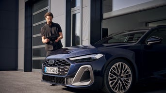 Ein Mann steht mit einem Tablet neben einem blauen Audi