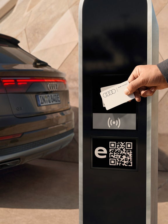 Ein Mann hält eine Audi Ladekarte an ein Terminal, im Hintergrund ein Audi Q8 SUV TFSI e.