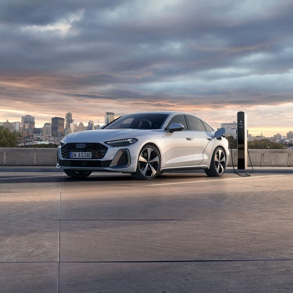 Sleek white e-hybrid car charging at a station, set against a city skyline at sunset.