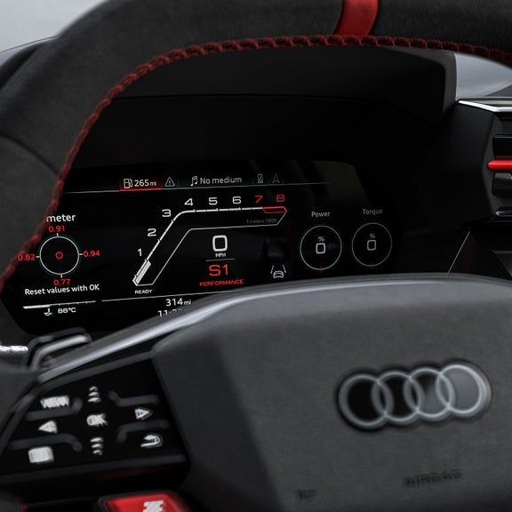 Close-up of a RS 3 Sportback car's digital dashboard showing speedometer, tachometer in red accents, and performance metrics on a sleek black background.