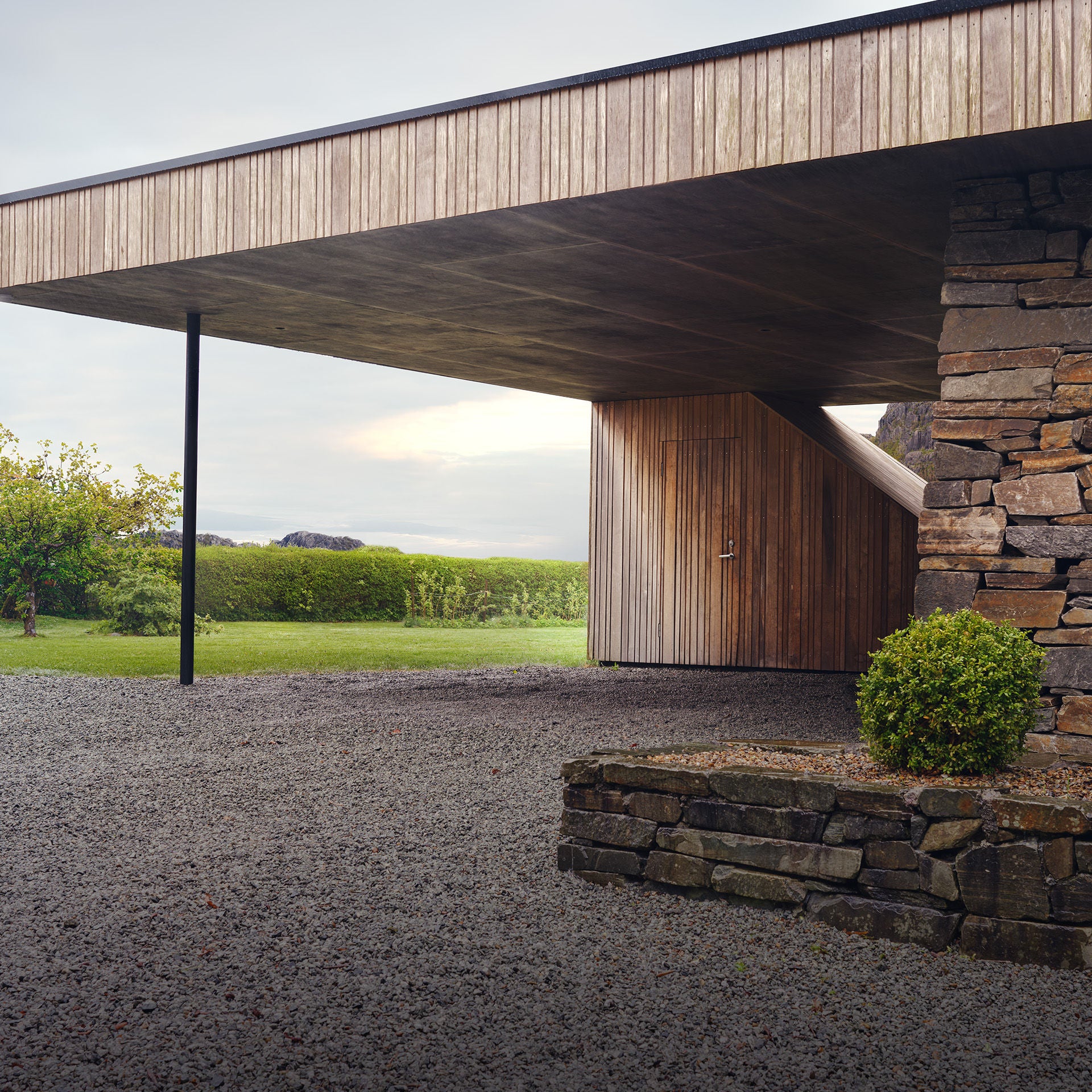 Corner view of a house with natural stone walls and a wood-panelled carport.