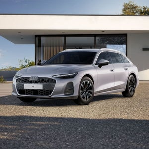 Une A6 Avant argentée est garée sur un parking en gravier devant une maison individuelle moderne.