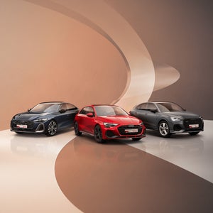 Drei Audi Fahrzeuge in Blau, Rot und Grau präsentieren sich nebeneinander auf einer glänzenden Oberfläche vor einem eleganten, geschwungenen Hintergrund in Beigetönen.
