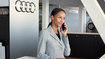 Eine Frau steht hinter einem Tresen bei Audi und telefoniert im Hintergrund die Audi Ringe.