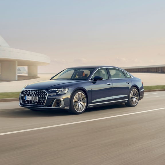 A  Audi sedan driving on the road with a modern building in the background.