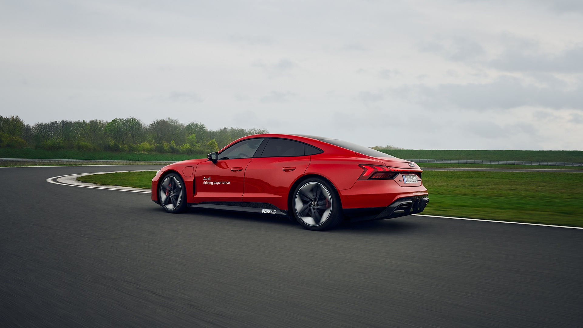 Roter Audi RS e-tron GT performance fährt durch eine Kurve auf einer Rennstrecke, Bäume und grauer Himmel im Hintergrund.