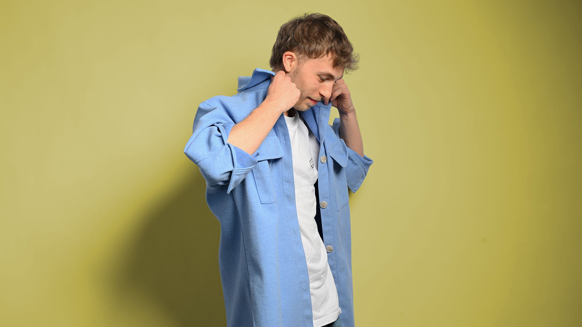 Julian schaut nach unten und richtet den Kragen seines blauen Hemdes