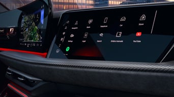 A close-up of a modern car dashboard featuring two digital screens with apps for navigation, music, and more, illuminated by red accents.