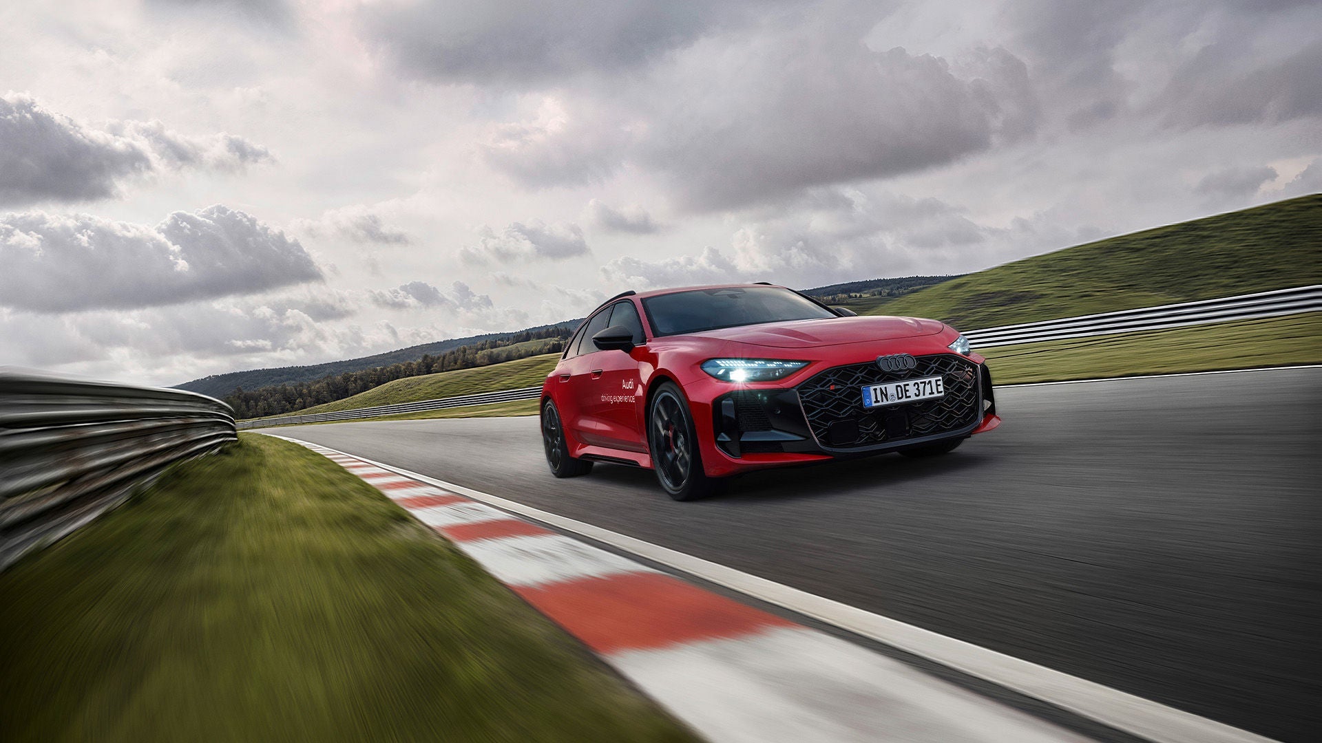Roter Audi RS 5 Avant fährt auf einer Rennstrecke; Bewegungsunschärfe, Leitplanken und wolkiger Himmel.