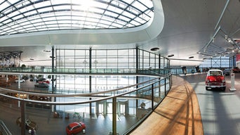 Große, lichtdurchflutete Ausstellungshalle mit Glasdach, mehreren Etagen und historischen sowie modernen Fahrzeugen.