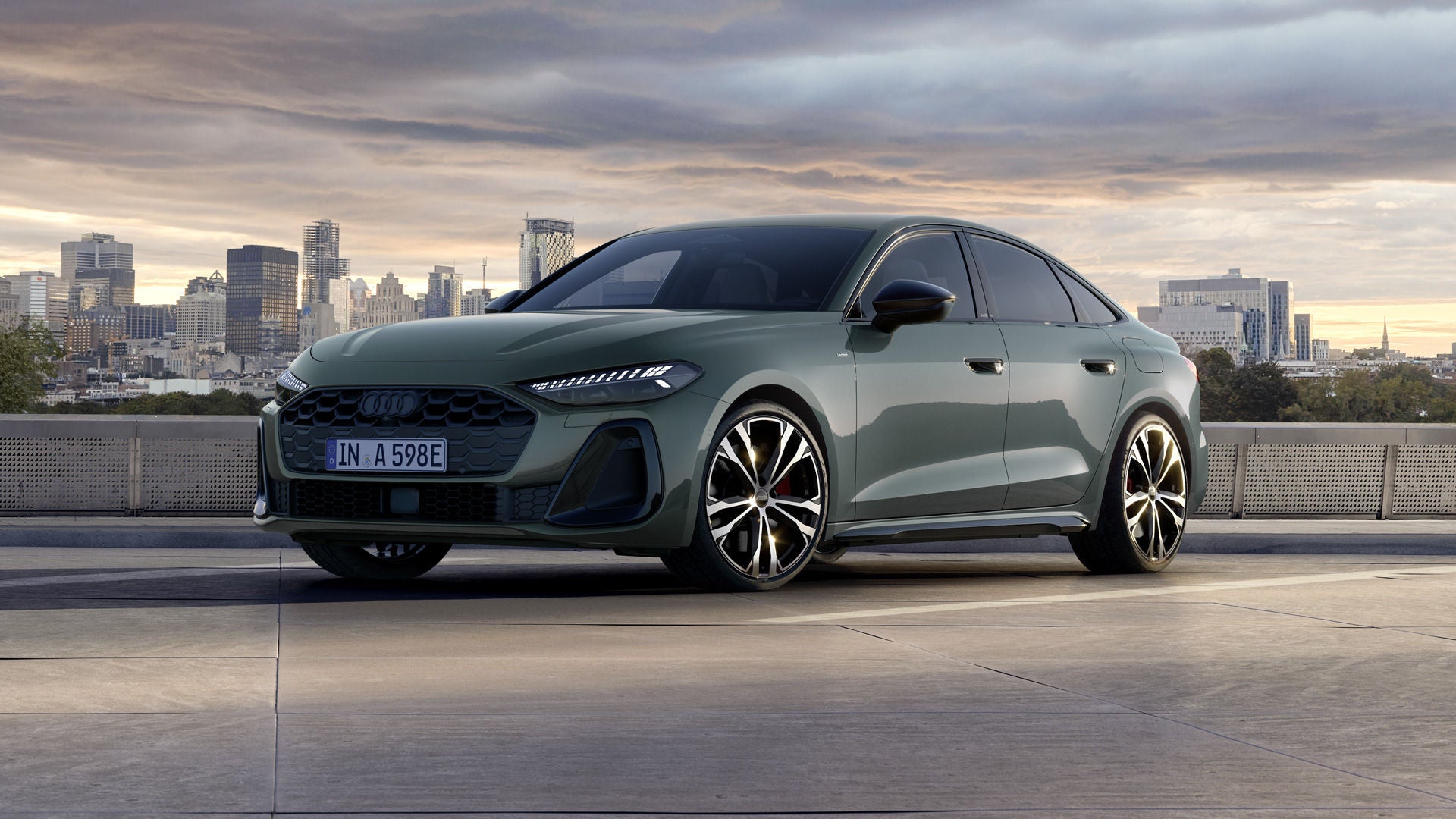 Die A5 Limousine e-hybrid mit Individuallackierung Camouflagegrün Metallic von schräg vorn. Im Hintergrund eine Großstadt-Silhouette.