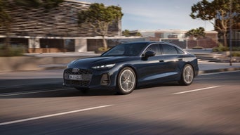 Fahraufnahme eines Audi A6 in der Stadt. Das Wetter ist gut. Im Hintergrund sind futuristische Gebäude zu sehen.