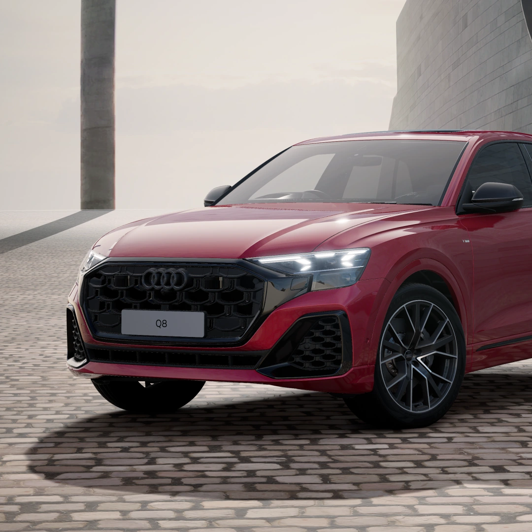 Front three-quarter view of a red Audi Q8 e-hybrid SUV in Vorsprung trim, parked on cobbled paving, with a black Singleframe grille and dark multi-spoke alloy wheels.