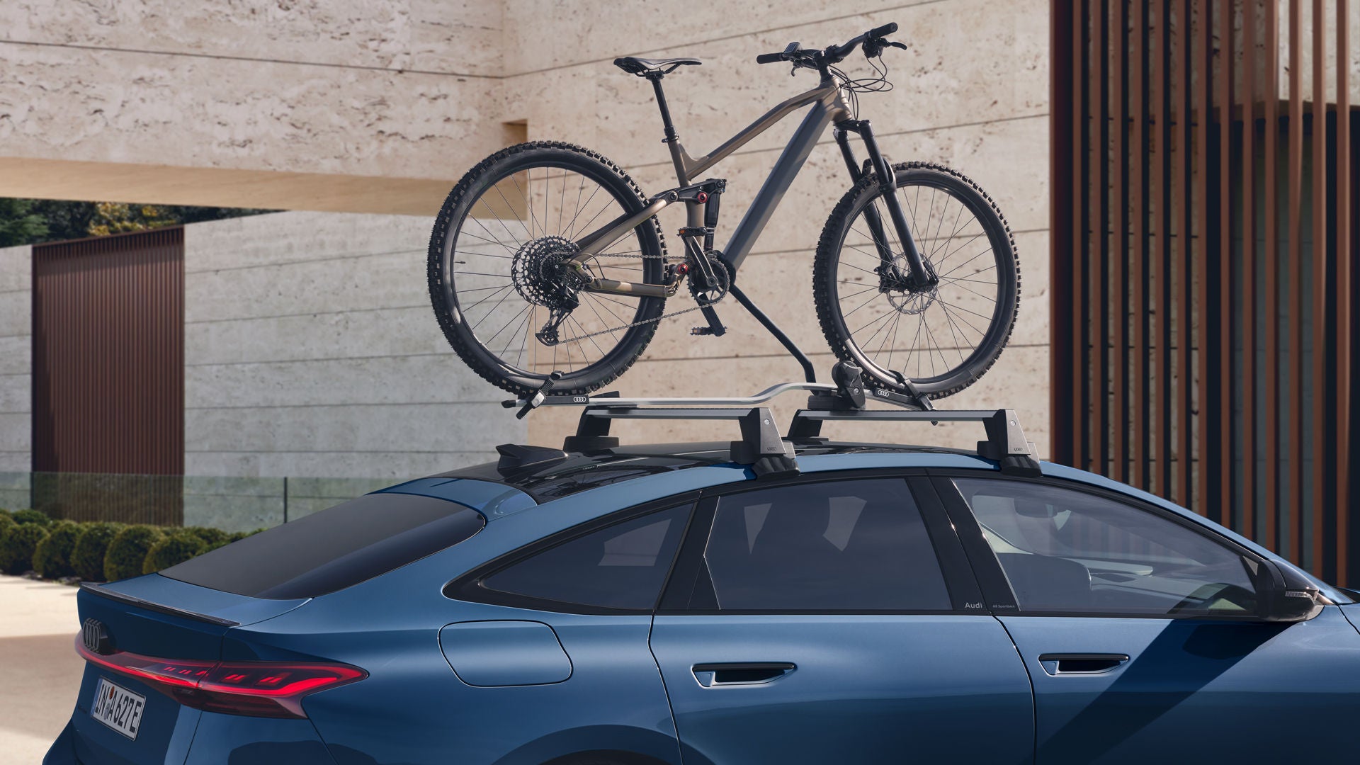 Der A6 Sportback e-tron im Anschnitt vor einem modernen Haus. Auf dem Dachgepäckträger ist ein Mountain Bike festgezurrrt.