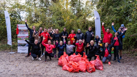 Gruppe posiert nach Plogging-Event mit vollen Müllsäcken
