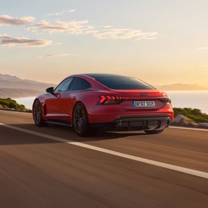 Der e-tron GT quattro auf einer kurvigen Küstenstraße bei Sonnenschein, zur Rechten das Meer, zur Linken felsiges Gebirge.