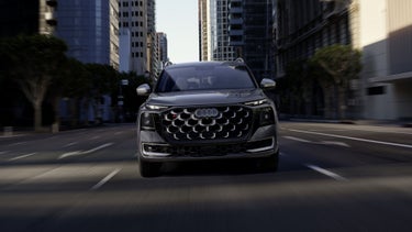 A front view of the Audi SQ9 SUV on an urban street, with skyscrapers in the background.