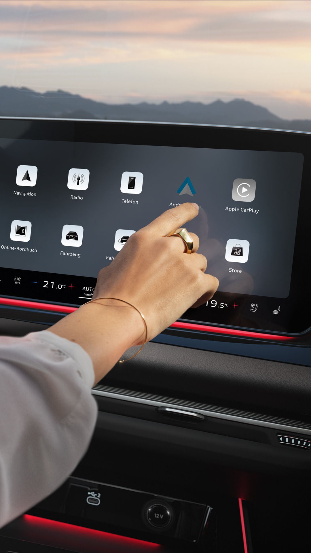 Detailaufnahme des Innenraum-Cockpits eines Audi: links das Lenkrad, in der Mitte ein beleuchtetes Display mit App-Icons. Ein Frauen-Arm ragt von links ins Bild und tippt auf das Display.
