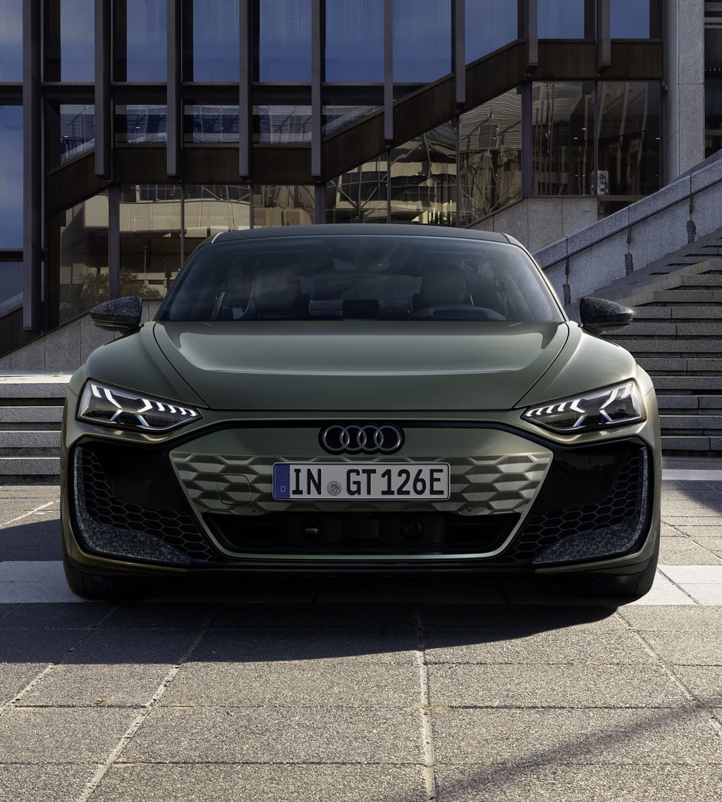Um Audi RS e-tron GT performance verde, visto de frente, em frente a um prédio moderno com escadas e fachada de vidro.