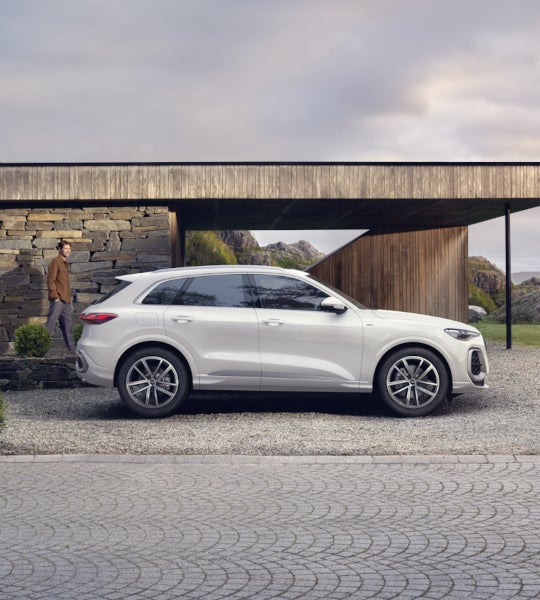 Een witte Q5 e-hybrid gezien vanaf de rechter zijkant staat voor een modern huis.