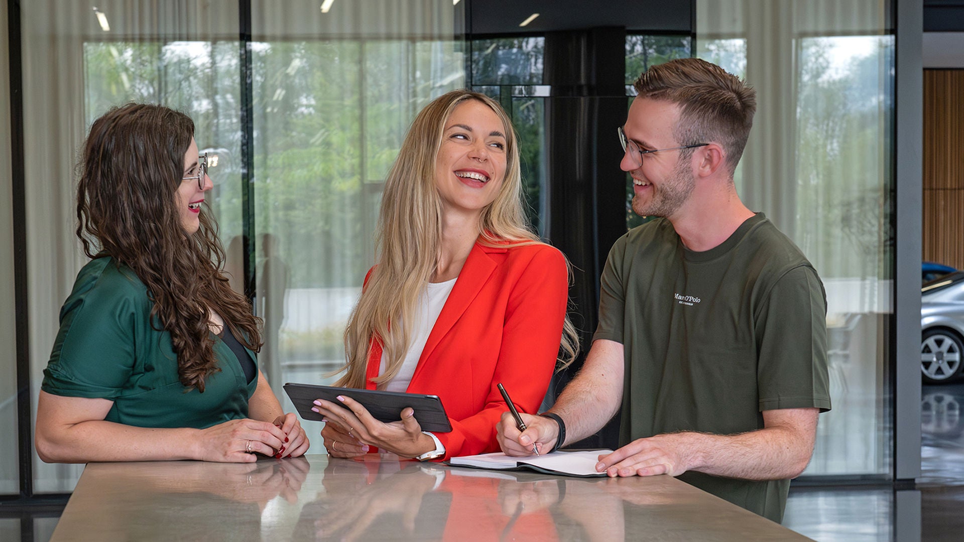 Zwei Frauen und ein Mann lachen miteinander und die mittlere Frau hält dabei ein Tablet in der Hand