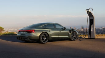 Grüner Audi RS e-tron GT performance lädt an einer Schnellladestation mit Stadtblick im Hintergrund.
