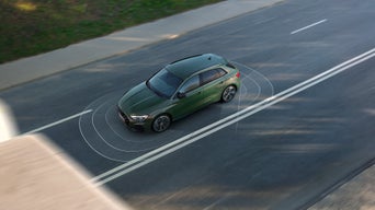 Ein grüner Audi fährt auf leerer Straße, digitale Linien zeigen Assistenzsysteme, Ansicht von schräg oben. 