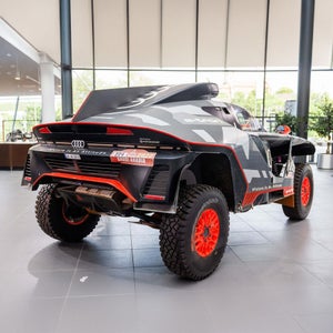 A black and red Audi off-road vehicle with large off-road tyres is on display in a brightly lit showroom.