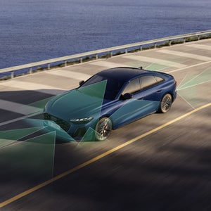 Die S5 Limousine von schräg oben, während sie auf einer Straße, am Ufer eines Gewässers entlangfährt. Vom Heck und der Front aus unterteilen grüne und blaue Vektoren die Flächen hinter und vor dem Fahrzeug.