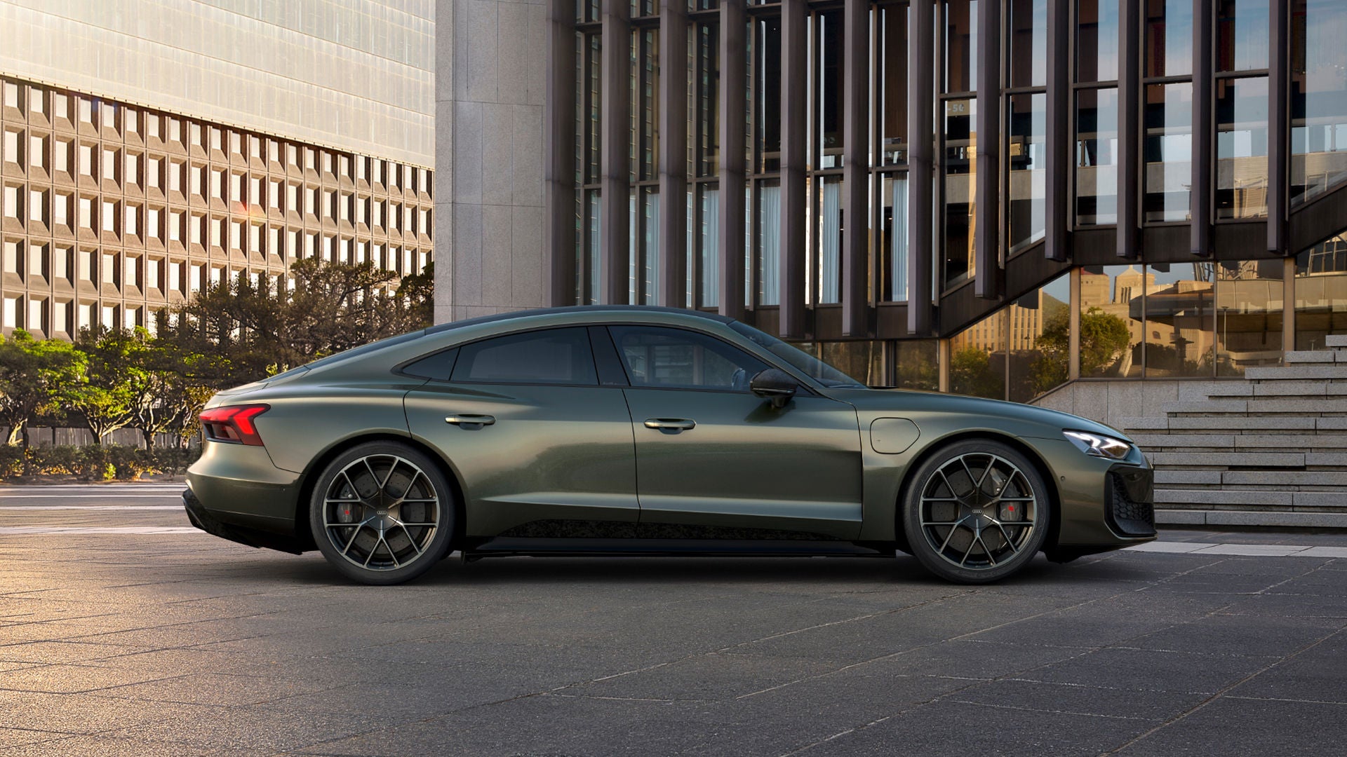 A green Audi car parked in an urban setting, with modern architecture in the background and stylish alloy wheels.