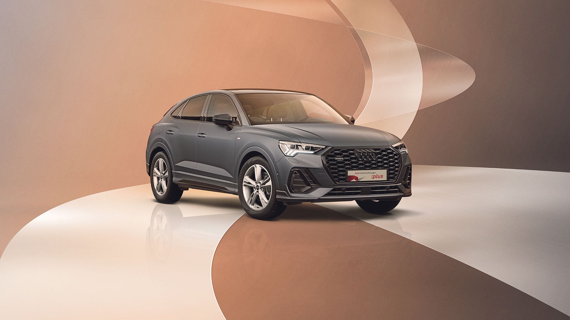 Ein grauer Audi Q3 steht auf einem modernen, bräunlichen Untergrund mit geschwungenen Dekoelementen.
