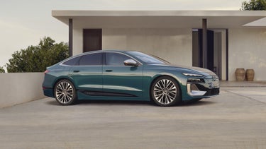 Der S6 Sportback e-tron steht im leicht schrägen Seitenprofil vor einem modernen Haus.