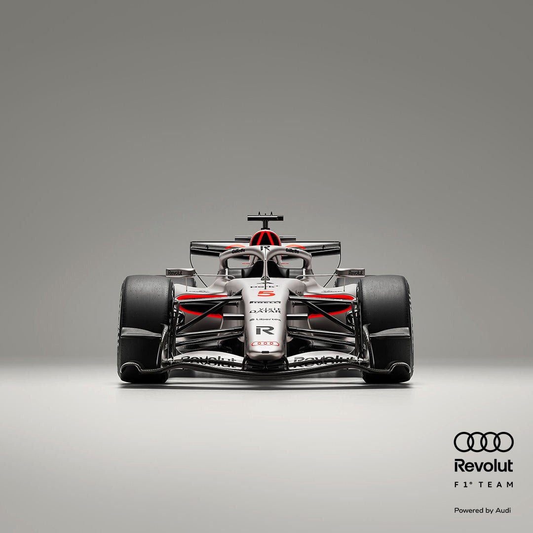 Frontansicht eines silber-schwarzen Formel-1-Rennwagens mit roten Akzenten vor grauem Hintergrund, Audi- und Revolut-Logo in schwarz am Rand.