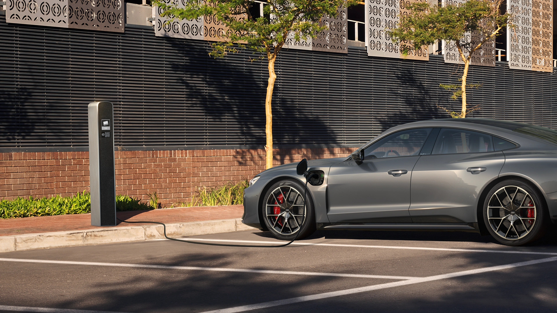 Grey electric car parked on road, charging from pillar on left.