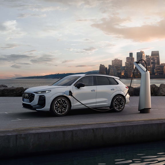 Audi Q3 SUV e-hybrid avec deux personnes prenant une photo avec leur téléphone portable. Il se tient de côté devant l'eau et se recharge.